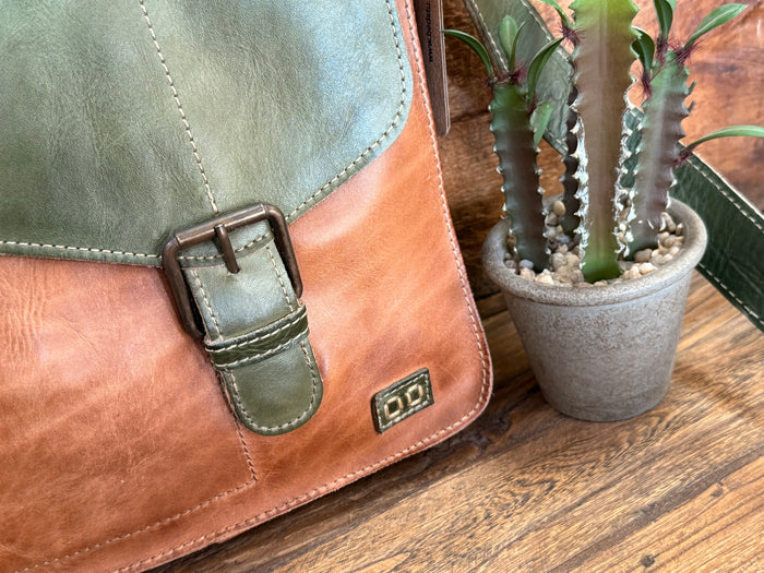 Close-up of green leather crossbody flap with tan panel, buckle strap and small logo.