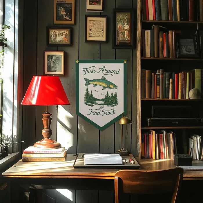 Wooden desk with books, red lamp, and Benoit’s Fish Around And Found Trout Felt Banner on wall for study decor.