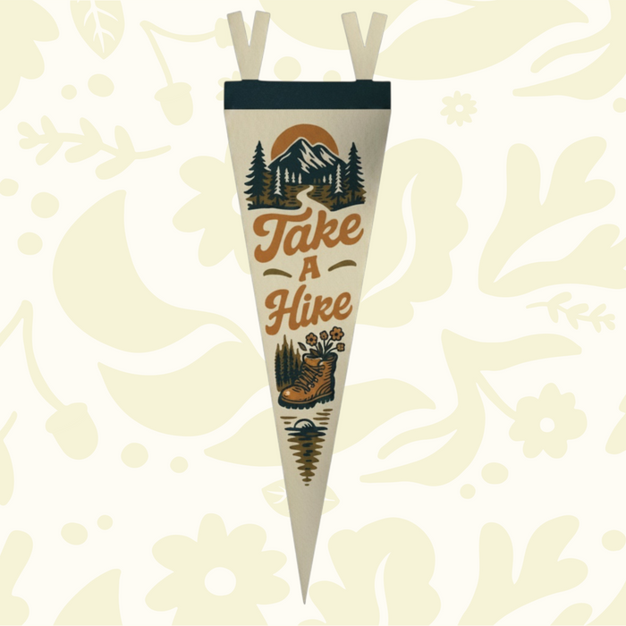 Forager Provisions LTD Take A Hike felt pennant featuring vintage mountain and hiking boot graphics on a wooden desk.