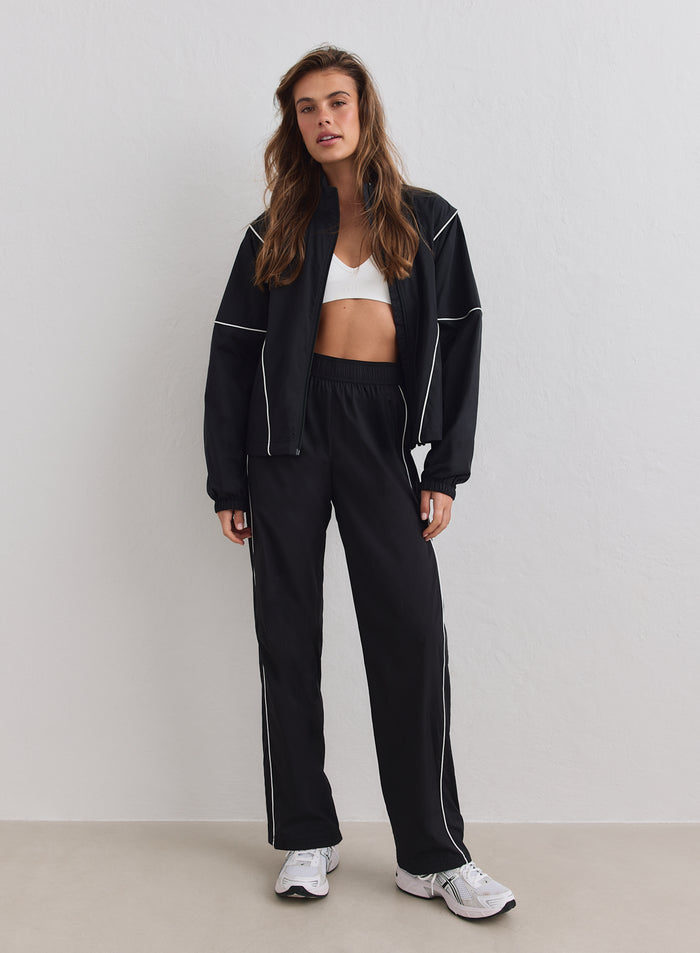 Musta aim'n Balance Windstopper Tracksuit Jacket valkoisilla tereillä, auki pidettynä urheiluliivien ja housujen kanssa.