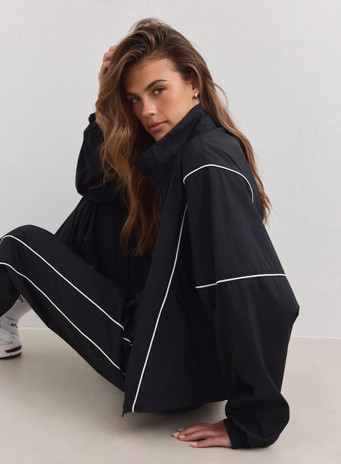 Nainen yllään musta aim'n Balance Windstopper Tracksuit -takki valkoisilla tereillä ja korkealla kauluksella.