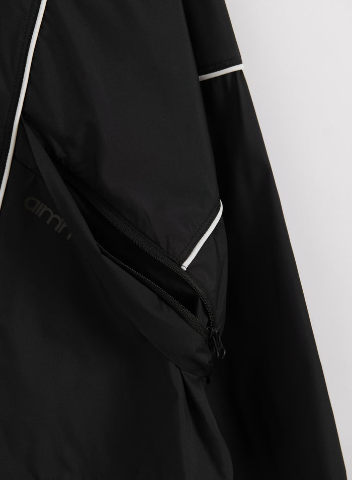 Musta Balance Windstopper Tracksuit Jacket -takki: vetoketjutasku, valkoiset tereet ja aim'n-logo.