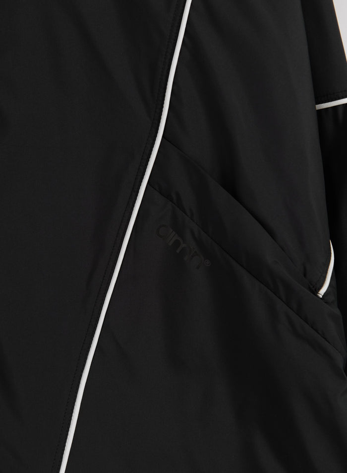 Yksityiskohta mustasta Balance Windstopper Tracksuit Jacketista valkoisilla tereillä ja sävy sävyyn olevalla aim'n-logolla.