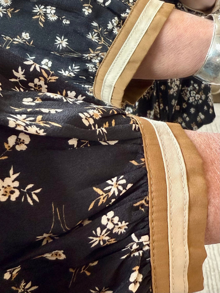 Black floral blouse sleeve close-up with tan contrast trim and cuff