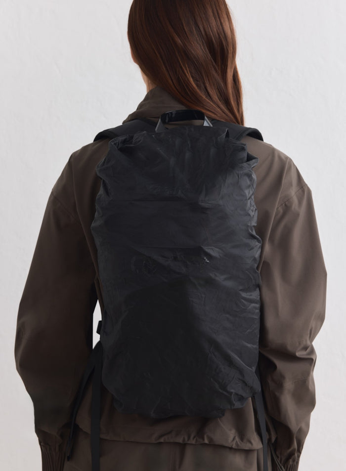 Musta aim'n Outdoor Daypack rypistetyllä polyesteripinnalla oliivinvärisen takin päällä.