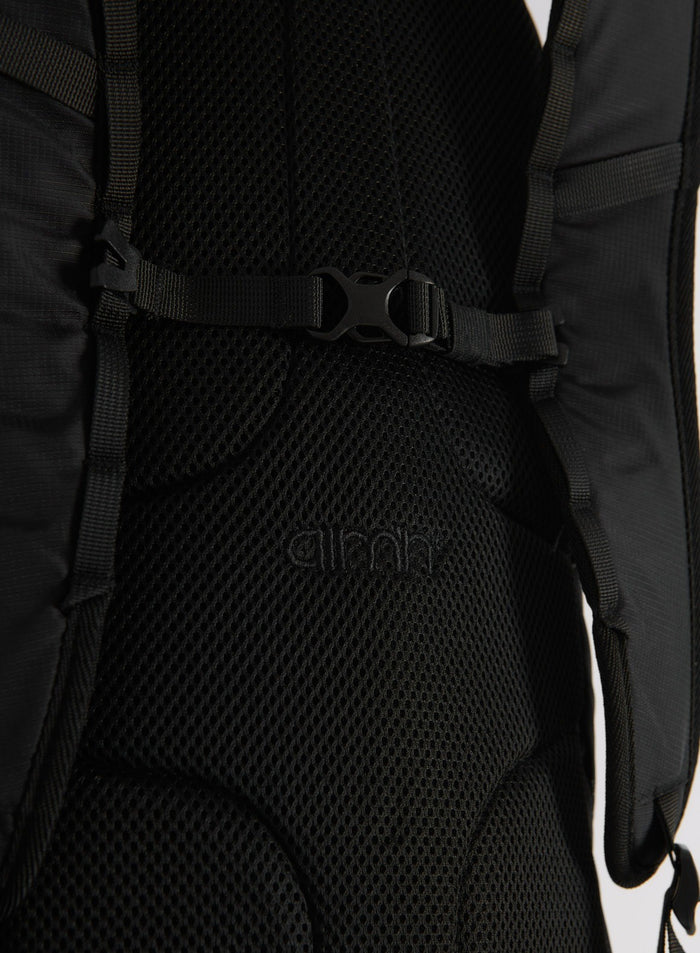 Lähikuva mustan Outdoor Daypack -repun selkäpehmusteesta ja hihnan soljesta, jossa näkyy aim'n-logo