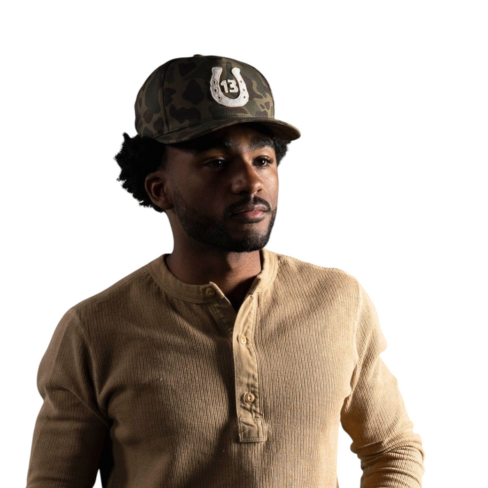 Forager Provisions LTD Bradley Mountain camo cotton twill cap with a raised 13 horseshoe patch worn by a man