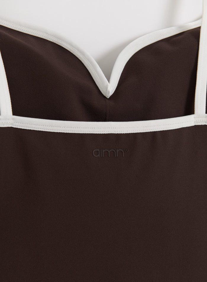 Lähikuva suklaanruskeasta Sense Contour Singlet -topista, jossa on valkoiset kontrastireunukset ja aim'n-logo.