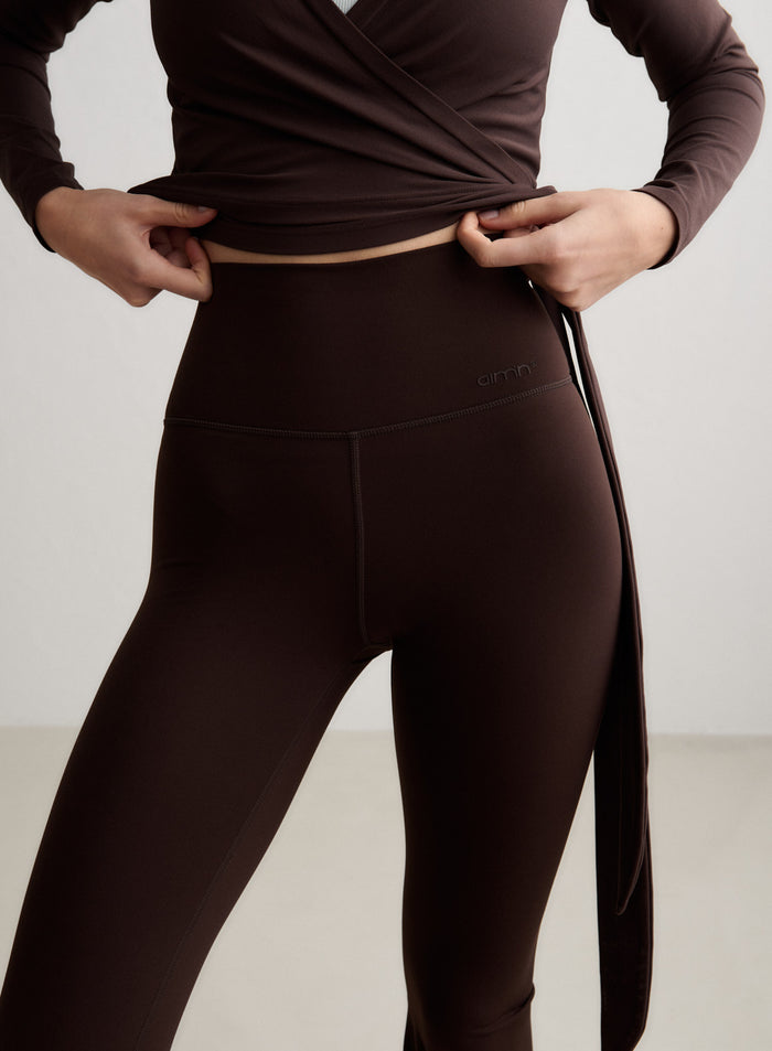 Suklaanruskeat korkeavyötäröiset Sense Flare Tall Tights ja yhteensopiva aim'n-kietaisupaita lähikuvassa. [S-174cm]