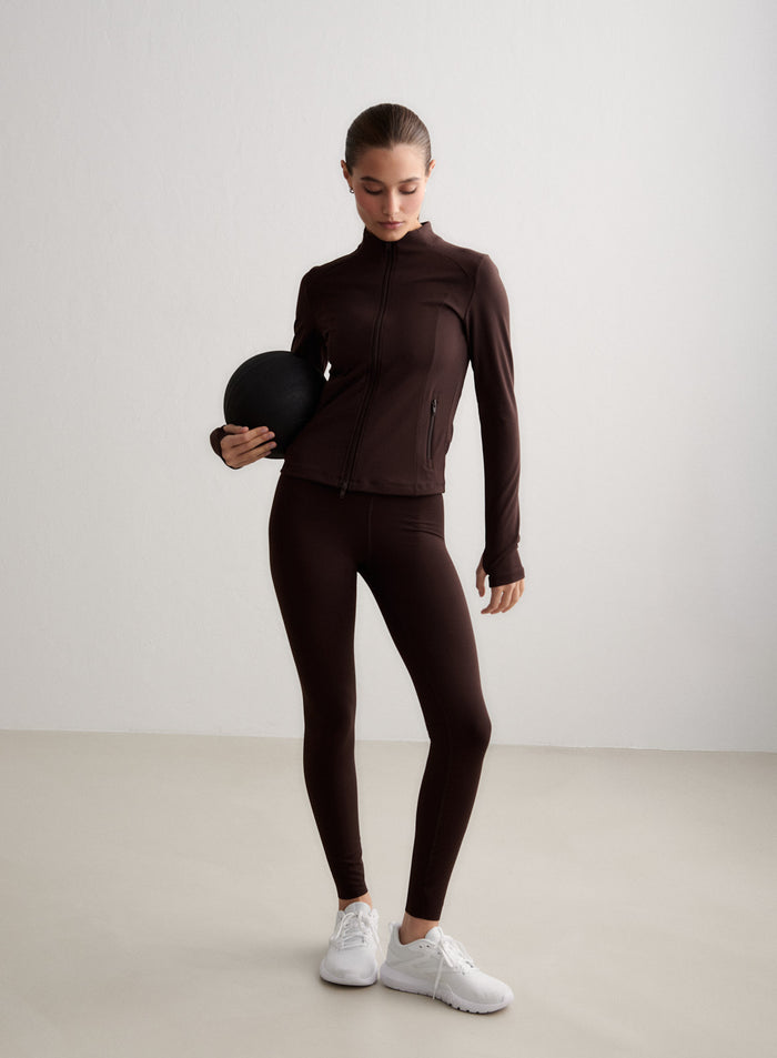 Suklaanruskeat aim'n Sense Tall Tights ja yhteensopiva takki kuntopalloa pitelevän mallin päällä. [S-174cm]
