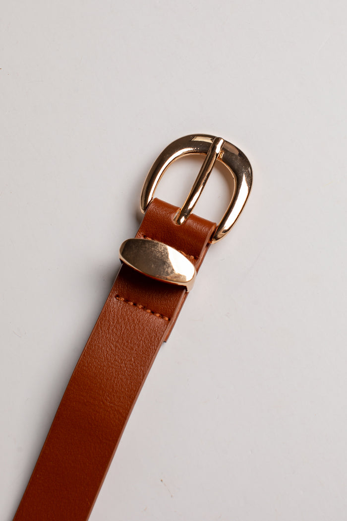 A close-up of a brown leather belt strap with a polished gold-tone metal buckle, resting on a light gray background.
