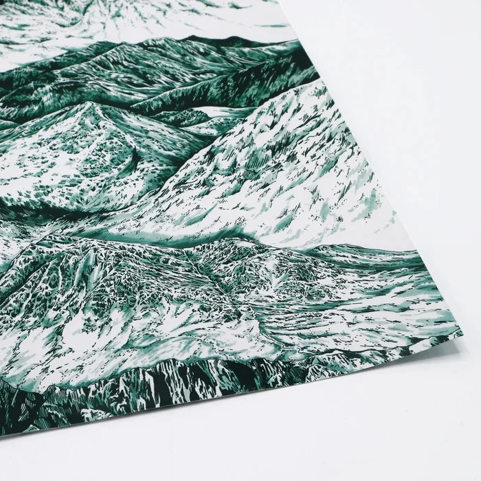 A close-up of a sheet of wrapping paper featuring a detailed, artistic illustration of mountain landscapes in shades of green and white, with the paper slightly curled at the edge."