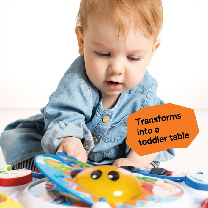 Baby playing with the Discovering Music Activity Table featuring piano, drum, guitar, and French horn instruments