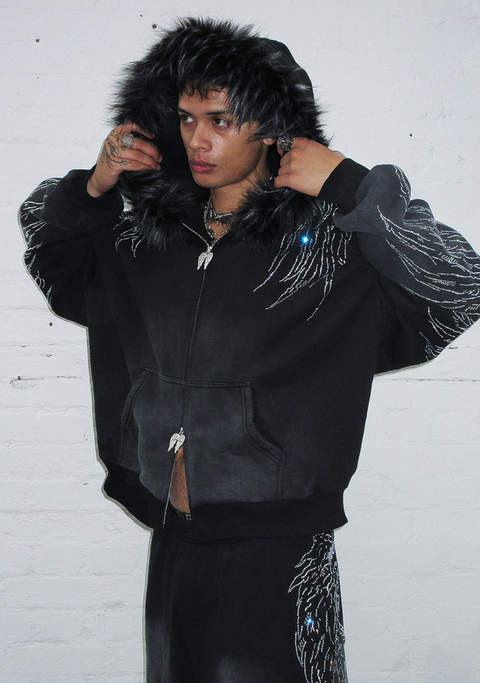 Model wearing a washed black zip hoodie with detachable fur and rhinestone wing design.