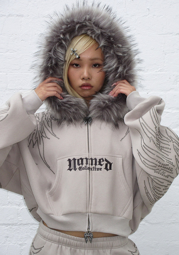 Model showcasing a bone hoodie with detachable fur hood and studded details on sleeves.