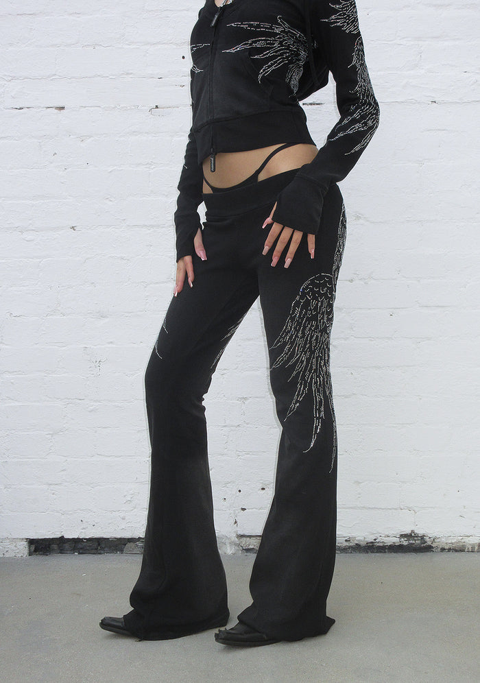 Model wearing washed black sculpt pants with rhinestone wing design, front view.