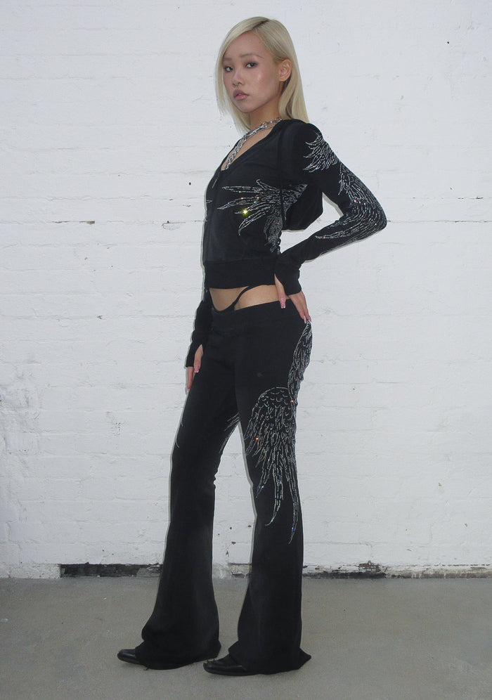 Model wearing a black hoodie featuring rhinestone wing embellishments and a deep v-neck design.