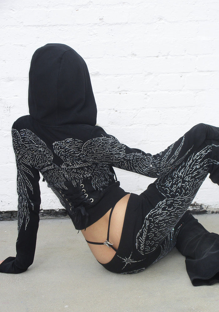 Back view of a black hoodie with rhinestone wings detail and black ribbon lacing at the lower back.