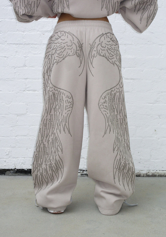 Back view of oversized bone sweatpants featuring studded detailing and adjustable ties at the ankles.