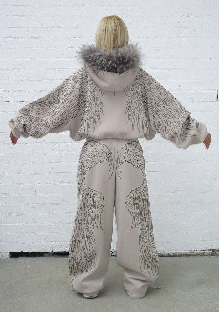 Model wearing oversized bone sweatpants with studded wing design and adjustable ankle ties, back view.