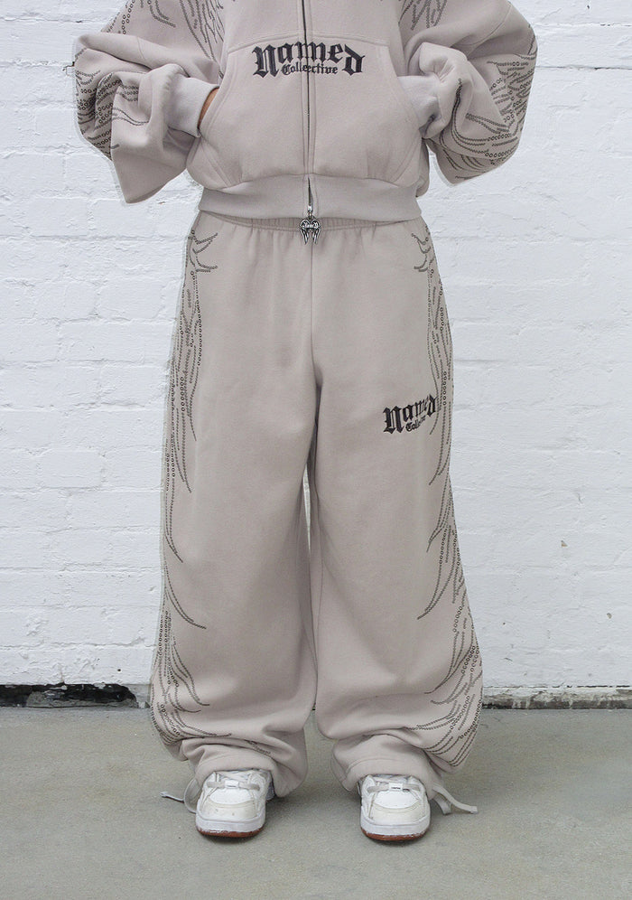 Model wearing bone sweatpants with studs and embroidered logo detail on the side in a front view.