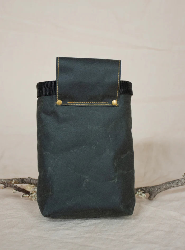 The Fernweh Sand/Scree waxed canvas chalk bag stands upright, branch behind, ideal for rock climbing and bouldering.