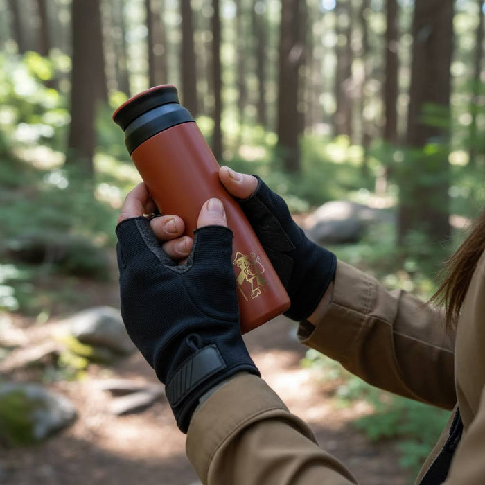 Forager Provisions Currant Berry Travel Mug held by gloved hands in a bright green forest, perfect for hiking or camping.