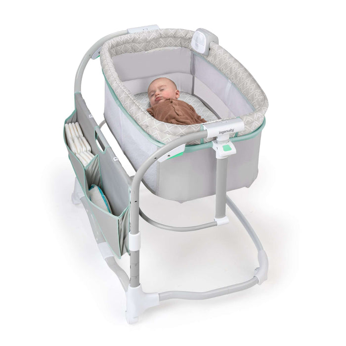 Ingenuity Dream & Grow Bedside Bassinet with breathable mesh sides and adjustable height next to a bed