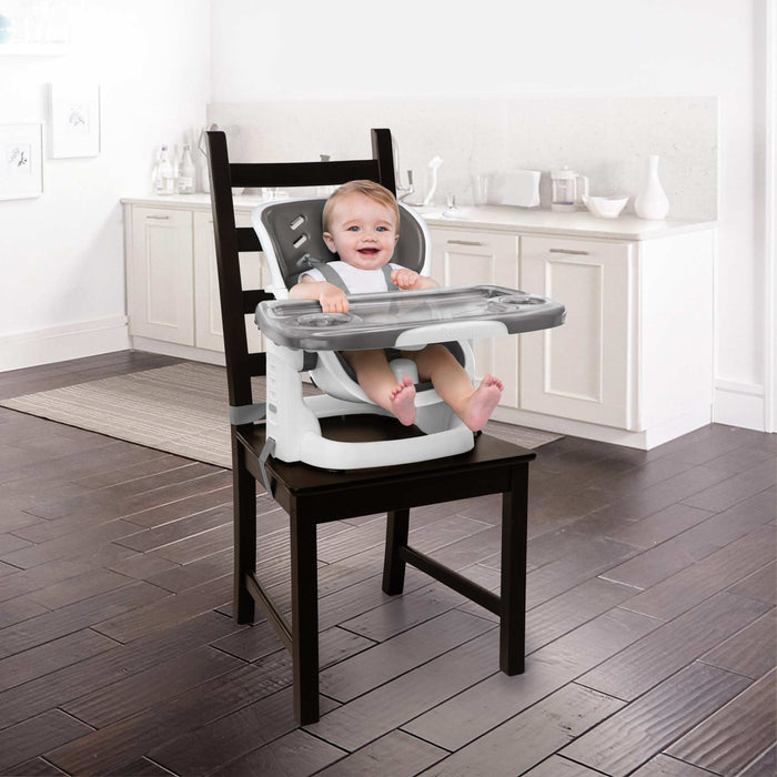 Ingenuity SmartClean ChairMate high chair and toddler booster seat in slate attached to dining chair with wipeable tray and safety straps