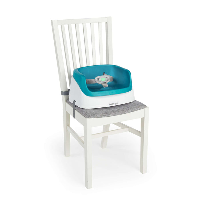 Ingenuity SmartClean Toddler Booster Seat in Peacock Blue attached to dining chair with 3-point harness and soft foam insert