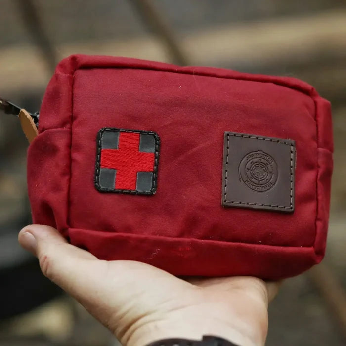 Hand holding Journeyman Craft First Aid Kit Belt, waxed canvas pouch with red cross patch, ideal for outdoor safety.
