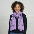 Woman wearing a purple scarf with butterfly pattern against a white wall.