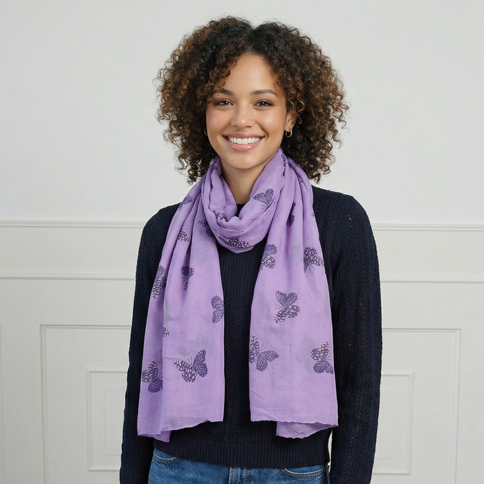 Woman wearing a purple scarf with butterfly pattern against a white wall.