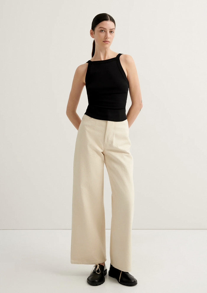 Woman wearing a black sleeveless top and beige wide-leg pants on a white background