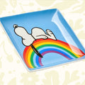 A blue box features a drawing of Snoopy lying on a rainbow, with text that reads "Magpie + Peanuts comic strip" at the top and "Good Vibes Trinket Tray" at the bottom.