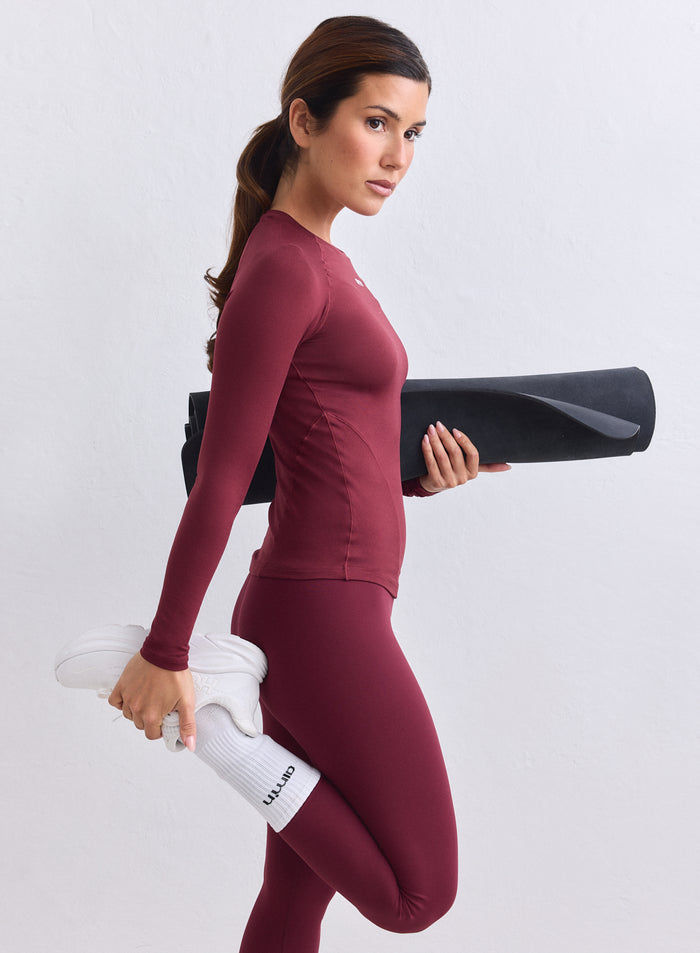Merlot Soft Basic Long Sleeve by aim'n yllään nainen venyttelee mustan joogamaton kanssa. [S-165CM]
