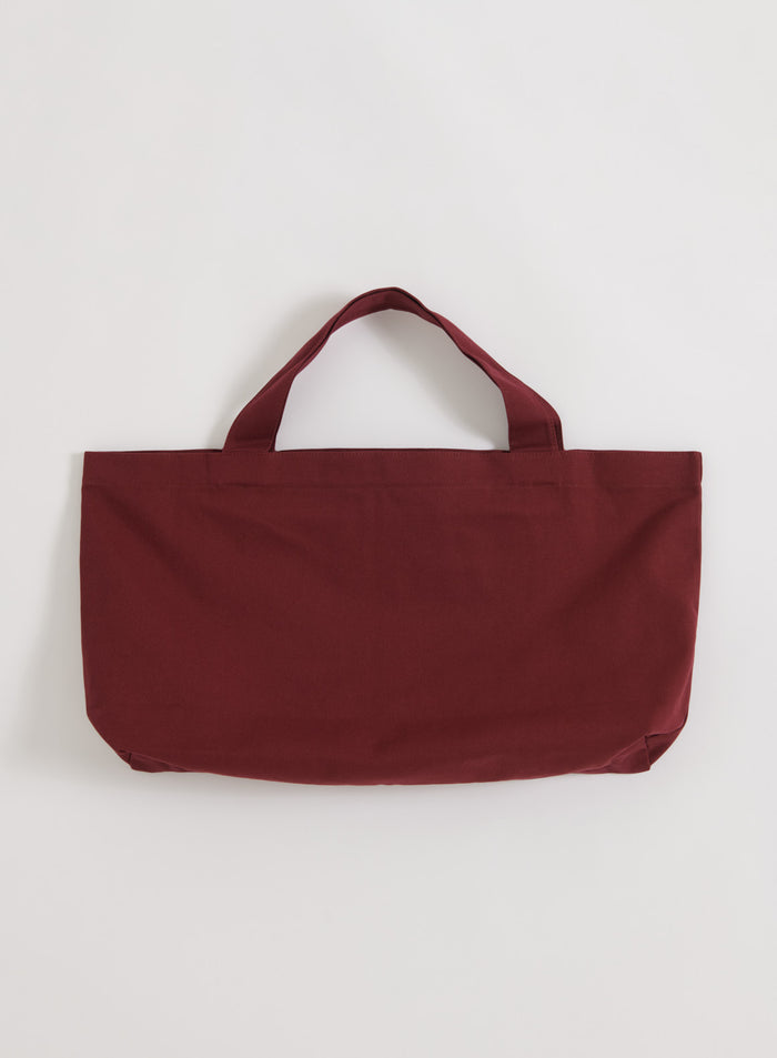 Täyteläisen merlot-punainen aim'n Varsity Tote Bag kudotusta puuvillasta flatlay-kuvassa.