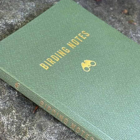 Green Mountaineers Books Birding Notes hardcover journal with gold binoculars logo on stone, perfect for birdwatchers.