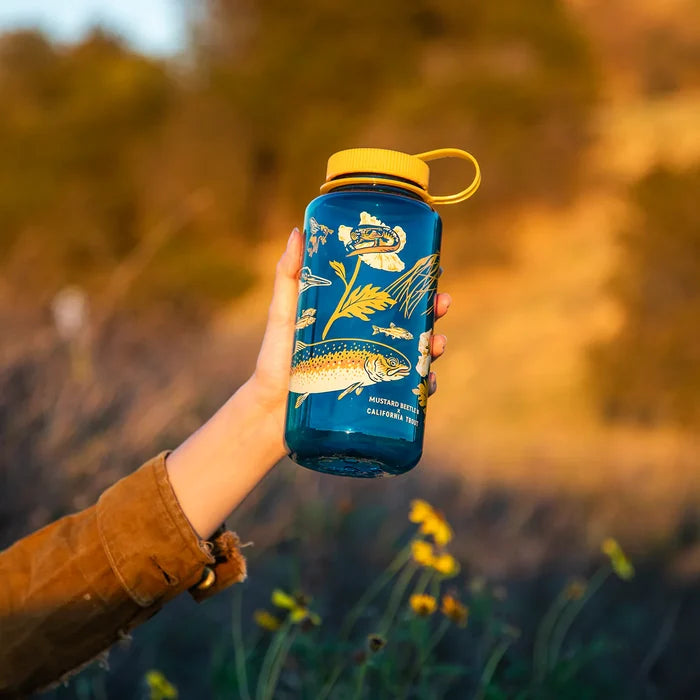 Hand holding Mustard Beetle 32oz Nalgene Malibu Creek bottle for Cal Trout outdoors, durable eco water bottle in nature.