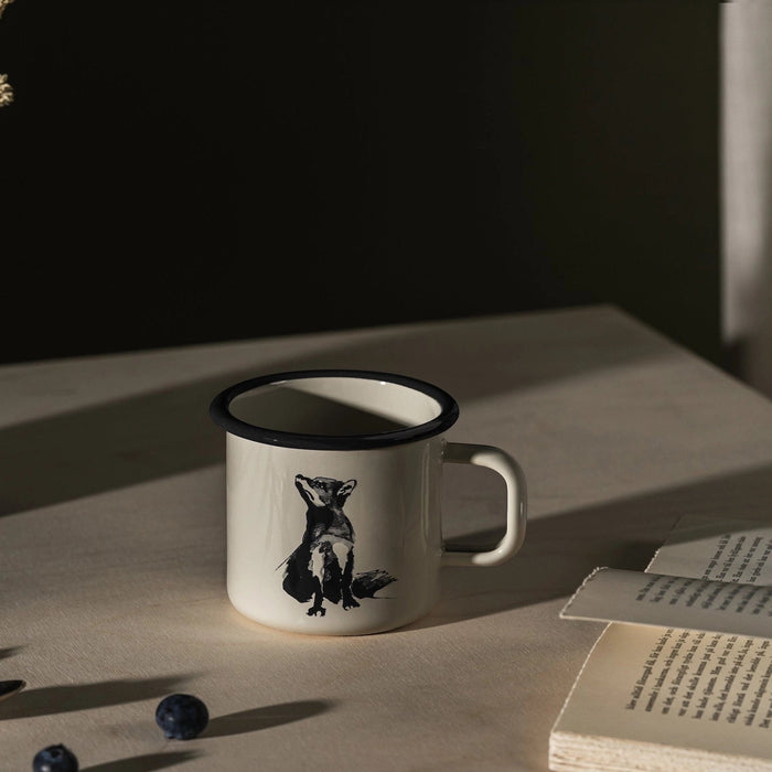 Muurla Teemu Järvi 0.37L Enamel Mug with Fox sits on table beside open book, fresh blueberries scattered, cozy kitchen scene.