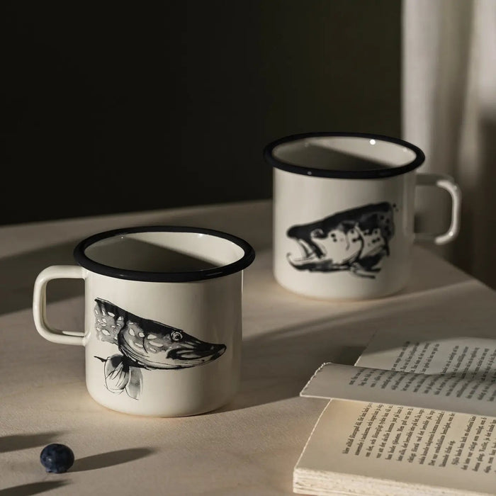 Muurla Teemu Järvi 0.37L Enamel Mug Pike & Trout on table with open book, fresh blueberry—unique Nordic homeware style.