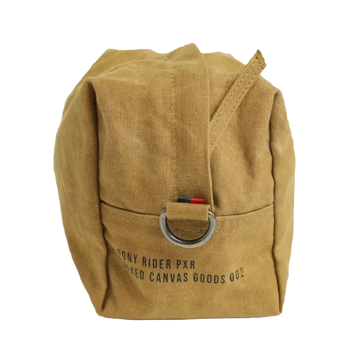 The Pony Rider Slow Road Waxed Canvas Toiletry Bag in Clay is a tan canvas grooming bag with a metal ring attached to a strap. It features the text "PONY RIDER PXR DYED CANVAS GOODS 002" printed on it. Made in India, this pouch comes with a handle zip closure for easy access and secure storage.