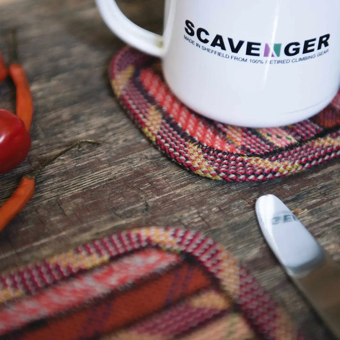 White mug on Scavenger Upcycled Fire Climbing Rope Coaster with knife, chili peppers, tomato on rustic wood background.
