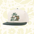 The Sendero Provisions LeRoy Brown Cap is a white and green cap made from durable cotton canvas, featuring an embroidered design of a fish and the text "Leroy Brown, Baddest in the Whole Town.