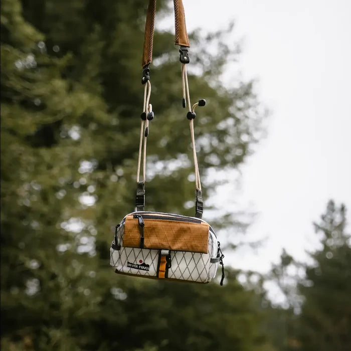 The Seven Peaks Fanny Pack in Brown, with compact two-tone style, stands out while hanging outdoors against lush green trees.