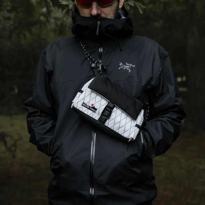 Outdoor person in black jacket wearing Seven Peaks Blanco Y Negro Riñonera Fanny Pack, visible logo, bold red dot design.