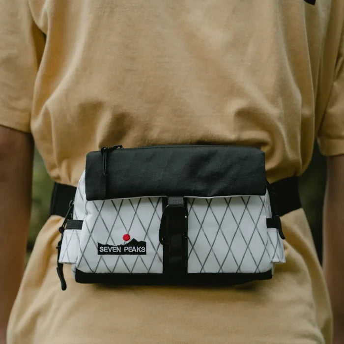 Beige shirt styled with a Seven Peaks Blanco Y Negro Riñonera fanny pack featuring a black and white diamond pattern.