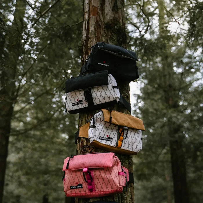 Backpacks in black, tan, white, and pink hang on a tree next to a Seven Peaks Blanco Y Negro fanny pack. Stylish bags.