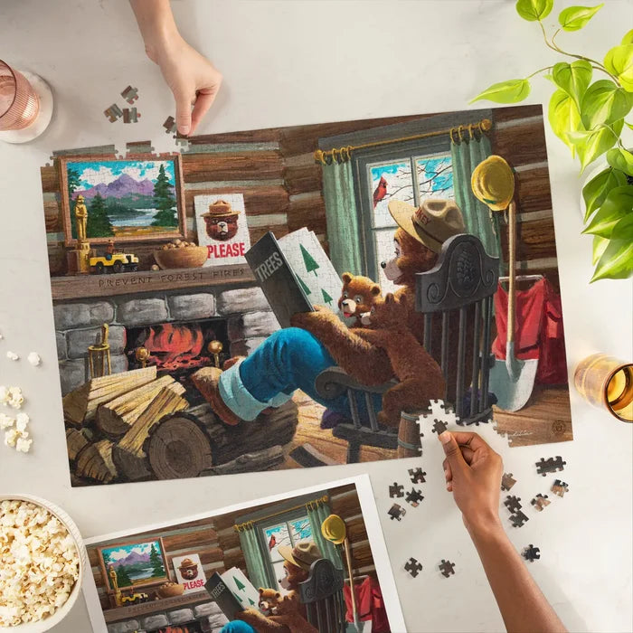 Three hands assemble Lantern Press Smokey Bear 1000 piece puzzle featuring Smokey Bear reading to cubs by a campfire.
