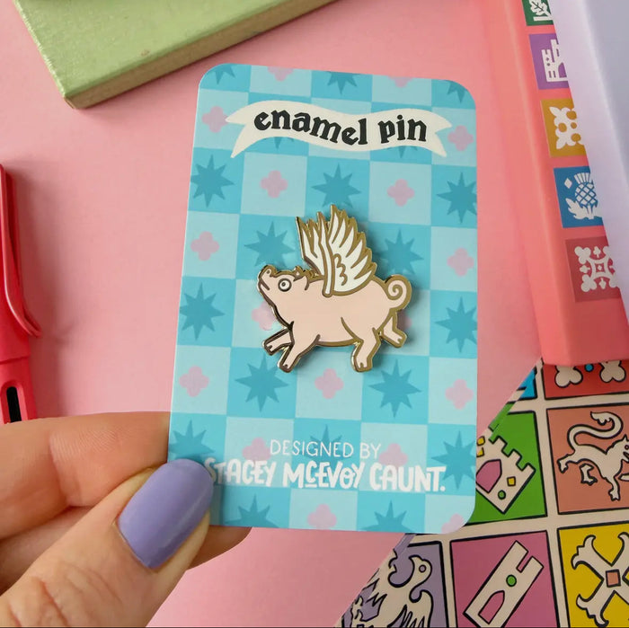 Forager Provisions LTD enamel pin featuring a whimsical pink flying pig with gold wings on a blue patterned card.
